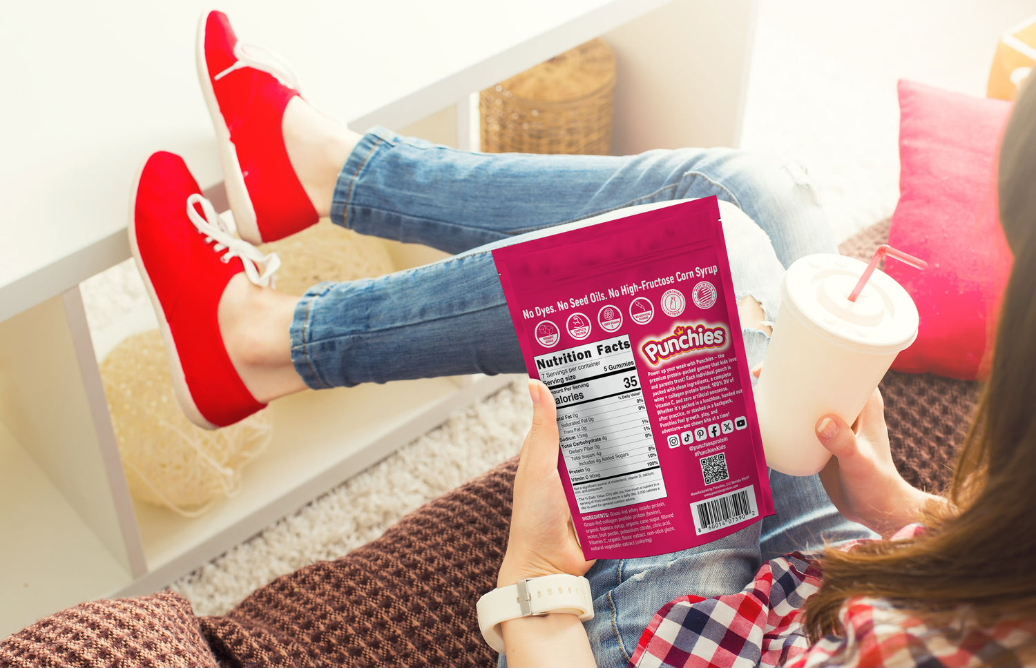 Person holding a box of Punchies candy and a drink, sitting on a couch.